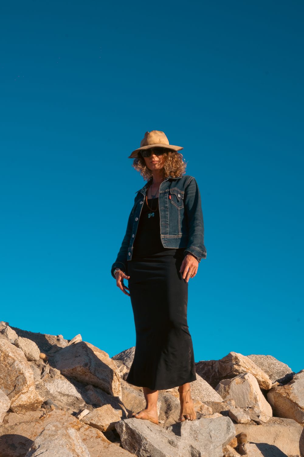 Elisabeth standing barefoot on rocks beneath a clear blue sky.